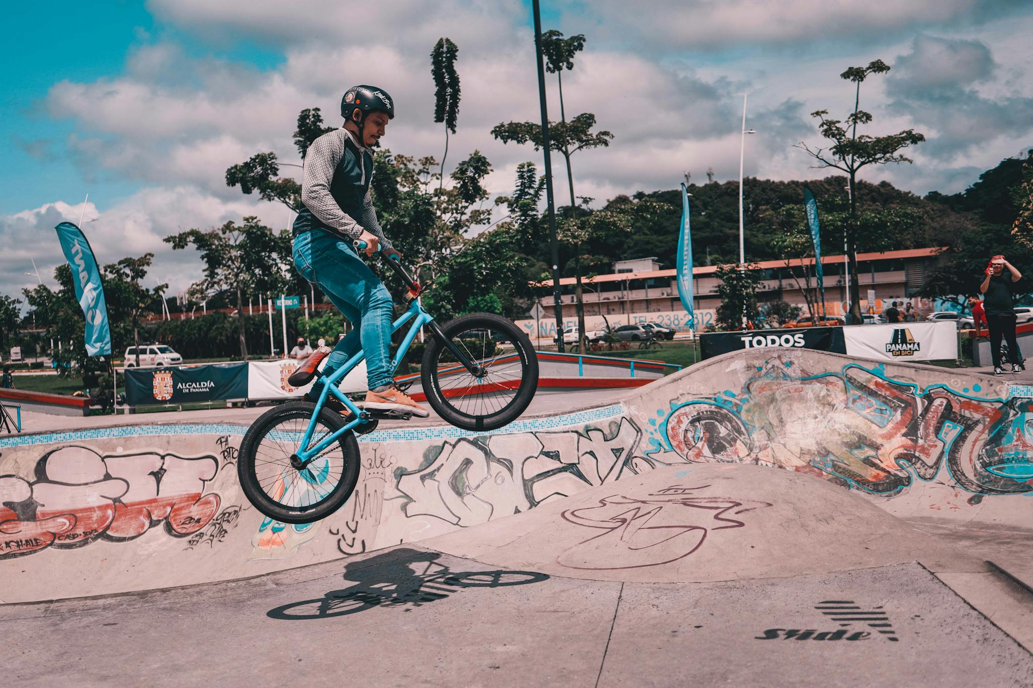 Dynamic shot of a BMX rider executing a jump in an urban skate park with graffiti walls under a cloudy sky.
